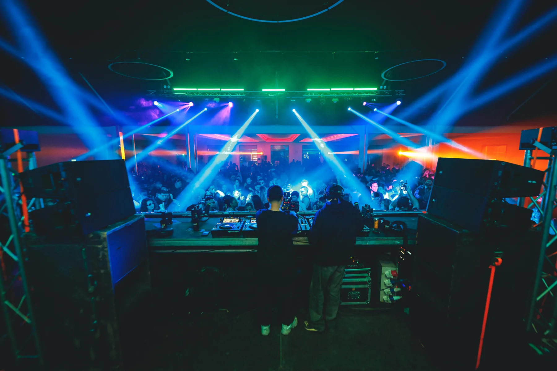 Set de DJ de Sunwave con haces azules y ámbar sobre el público en un evento nocturno